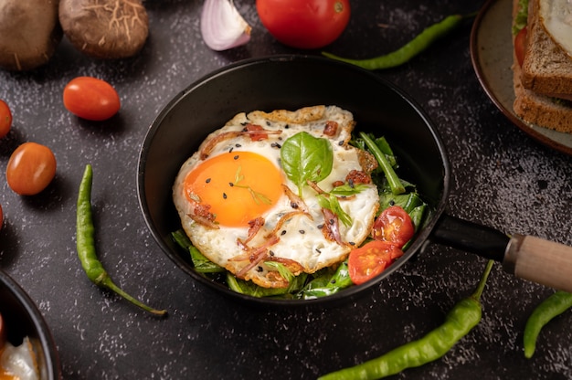 Free photo breakfast with fried eggs, sausage, and ham in a pan with tomatoes. chili and basil.