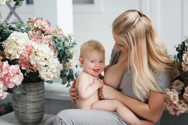 Free photo breastfeeding baby sitting on laps in studio room decorated with flowers.