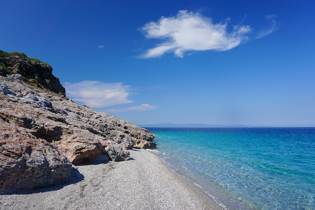 Breathtaking shot of a blue sea meeting with a sunny rocky beach under the blue sky