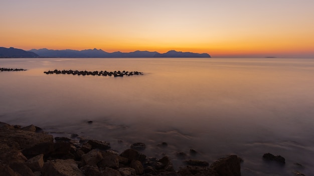 Free photo breathtaking shot of the calm sea and rocky shore during sunset