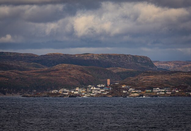 Breathtaking shot of a deep blue ocean and a small town below a mountain range on a cloudy day