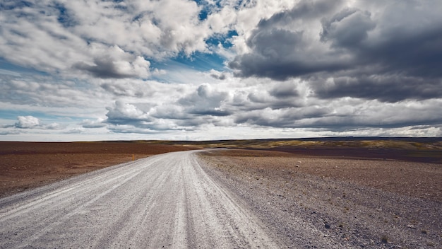 Free photo breathtaking shot of a secluded road stretching through a beautiful field under the cloudy sky