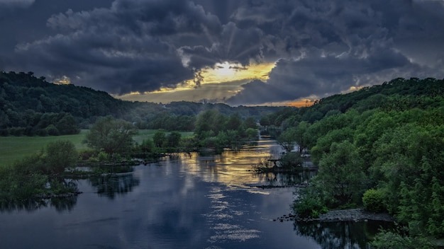 Free Photo breathtaking susnet at a river in the middle of a green forest under the dark sky