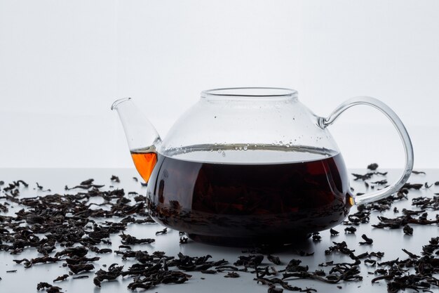 Brewed tea in a glass teapot with dry black tea side view on a white surface