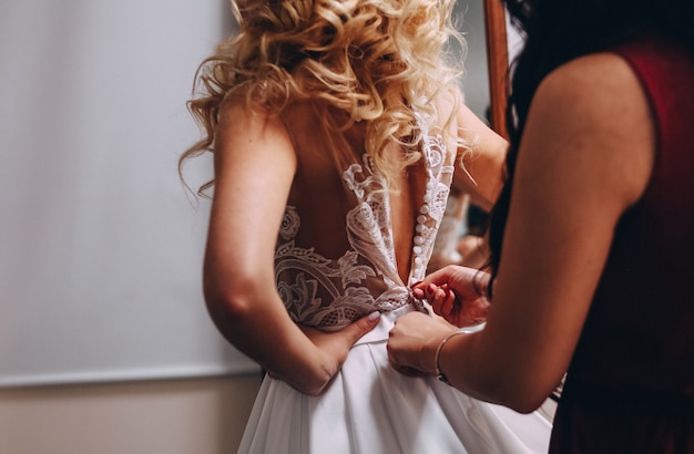 Free photo bride blonde dresses a beautiful dress a woman helps her button up on the back