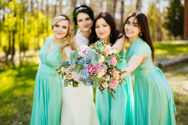 Bride and bridesmaids with wedding bouquets. Sunny wedding reception joyful moment.