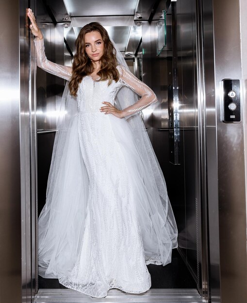 Free photo bride in gown posing against the background of metal elevator doors