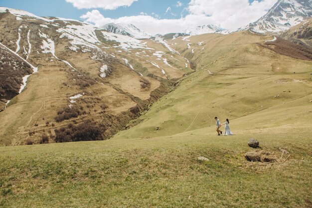 bride and groom are walking on the grass in summer in high mountains