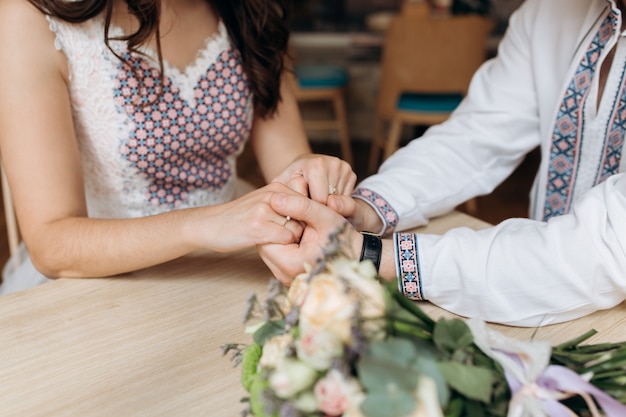 Bride and groom in ethnic clothes hold each other hands sitting