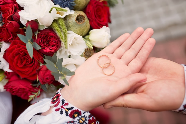 Bride and groom hold wedding rings in their arms