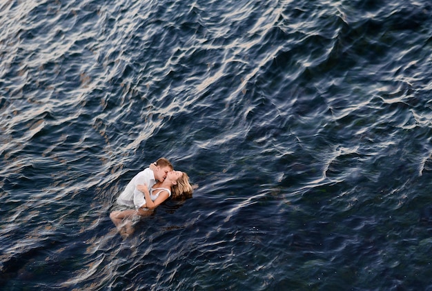 Free photo bride and groom hugging in ocean water and kissing