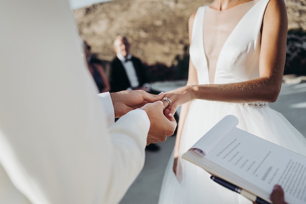 Bride and groom in light summer clothes hold each other hands during the ceremony