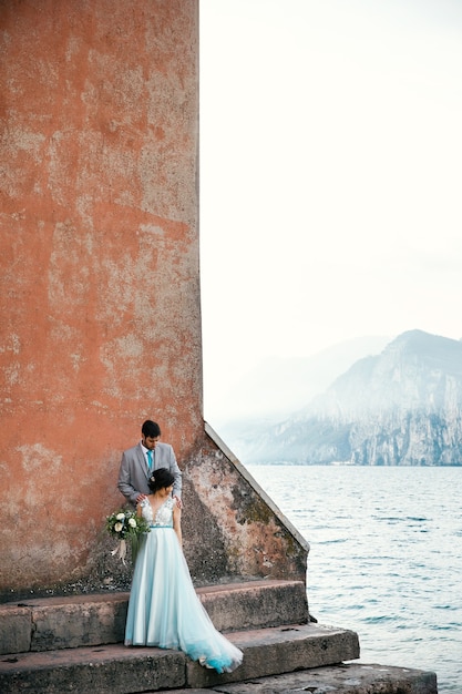 Bride and groom stand together on the shore before the sea