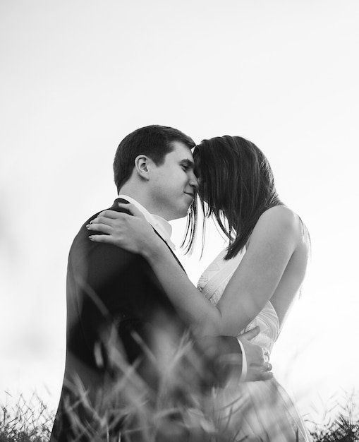 "Bride and groom standing in field hugging"