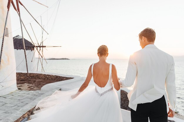 Bride and groom walk towards the sunset over the sea