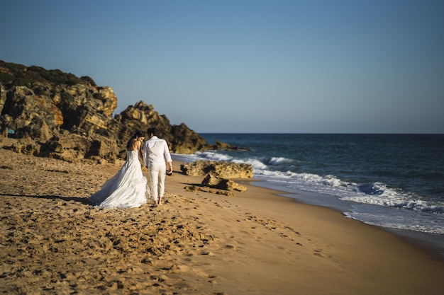 Bride and the groom walking at the sandy beach