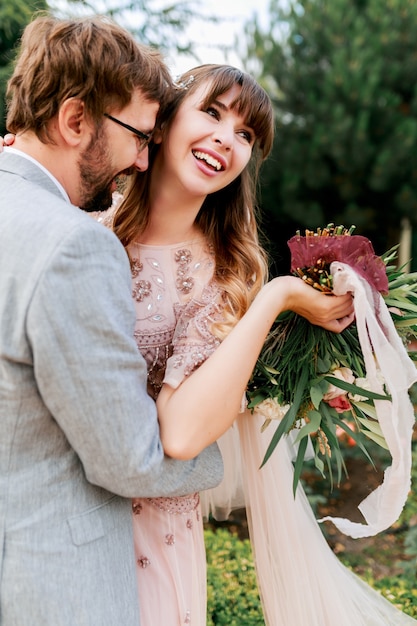 Bride and groom at wedding Day walking Outdoors on spring nature. Happy Newlywed woman and man embracing in green park. Loving wedding couple.