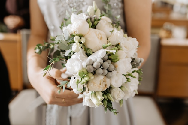 Bride holds the beautiful bridal bouquet with white peonies and green decor