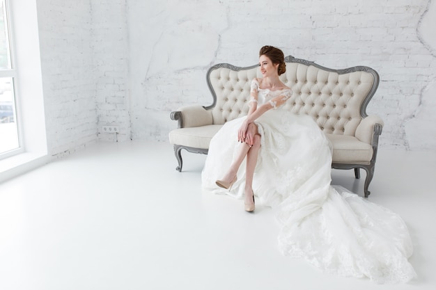 Bride looking out the window, she waits for the groom sitting on big classic sofa. 