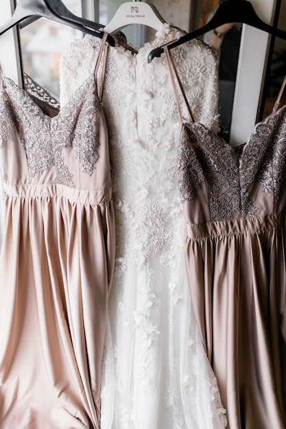 Free photo bride's dress and her two bridesmaids dresses are hanging on hangers