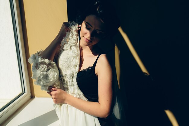 Free Photo bride sitting on a windowsill and holds wedding dress