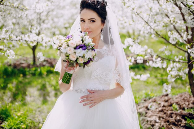 Bride smelling her bouquet with flowering trees background