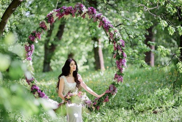 Bride with long dark hair sits on a large circle of lilac