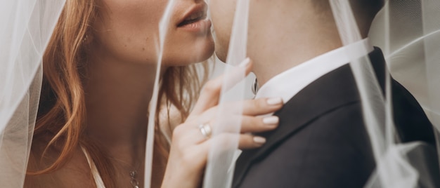 Free photo bride with red hair kisses groom standing under the veil