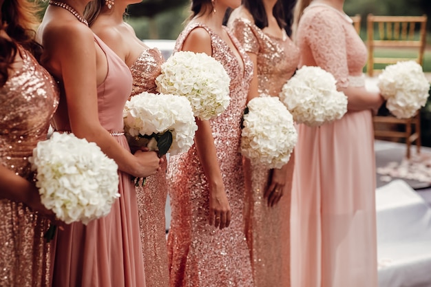 Bridesmaids in pink dresses stand with white flower bouquets in