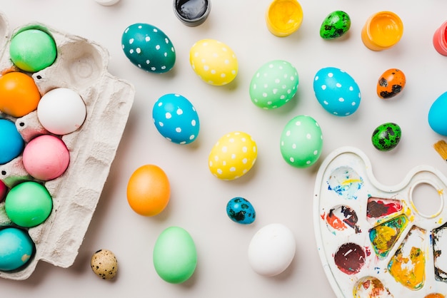 Bright collection of colored eggs near container, water colors and palette