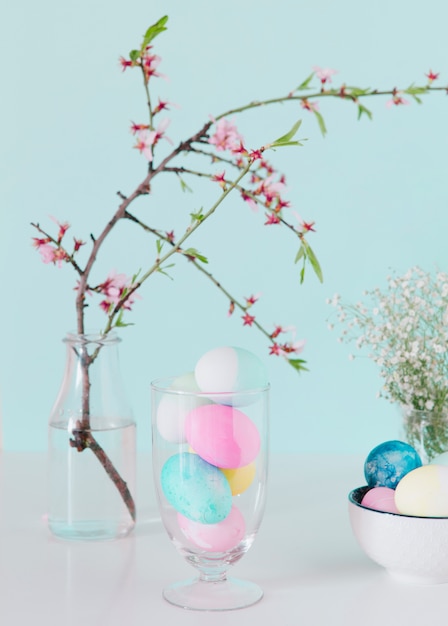 Free photo bright easter eggs near flower twig in vase with water and bowl