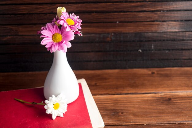 Bright flowers in white vase on book 