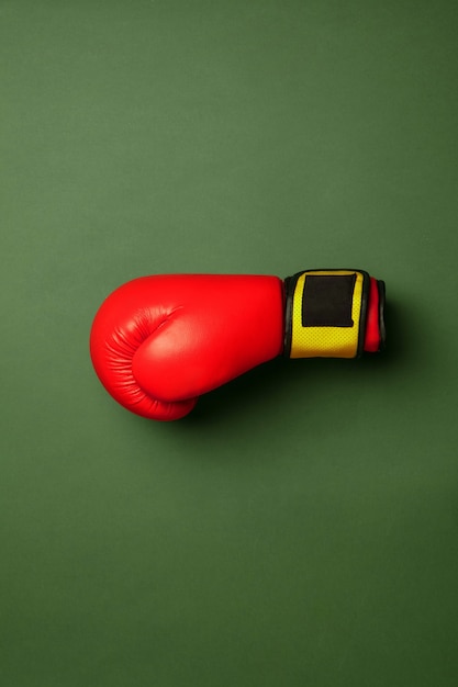 Free photo bright red and yellow boxing glove. professional sport equipment isolated on green studio background. concept of sport, activity, movement, healthy lifestyle, wellbeing. modern colors.