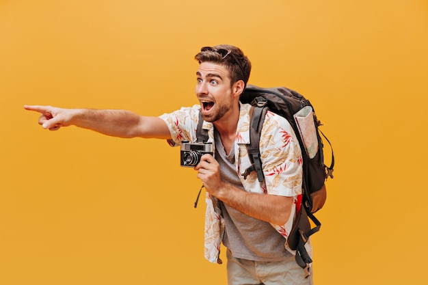 Free photo bright tourist with ginger beard in white cool shirt and grey t-shirt showing aside his finger and holding camera on isolated wall