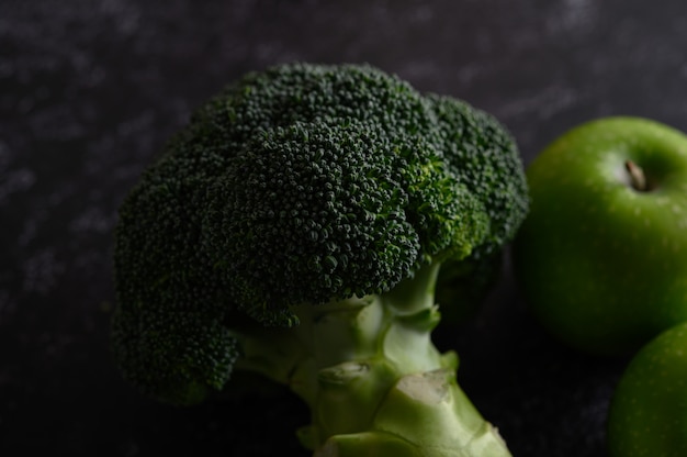 Free photo broccoli, apple, and avocado on a black cement floor.