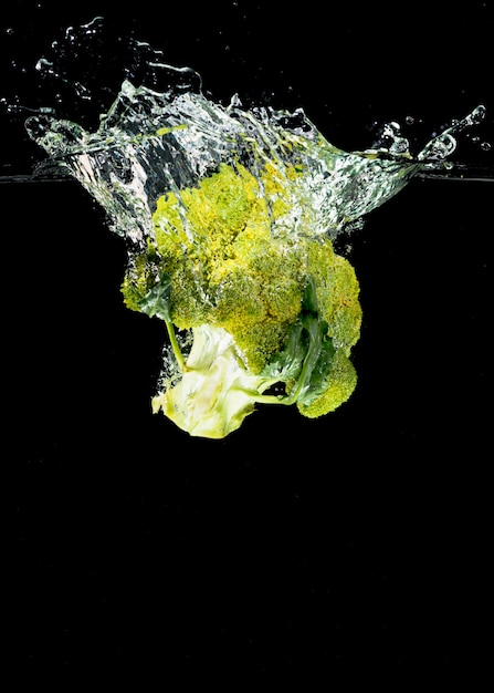 Broccoli falling in water against black background