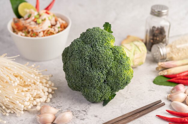 Broccoli, golden needle mushroom, chopsticks, garlic and chilies on a white cement floor