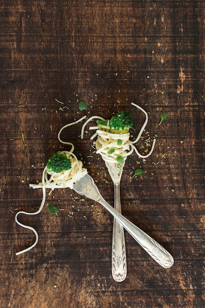 Free photo broccoli with noodles on crossed fork against wooden textured backdrop