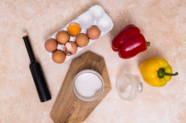 Broken eggshells; oil bottle; sugar jar and bell peppers on textured backdrop