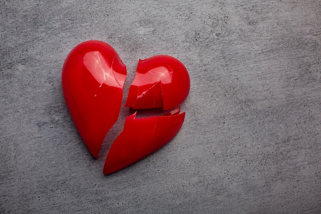 Broken plastic red heart on grey background