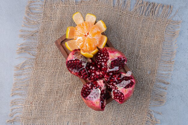 A broken pomegranate and a peeled tangerine on a piece of cloth on marble background. 