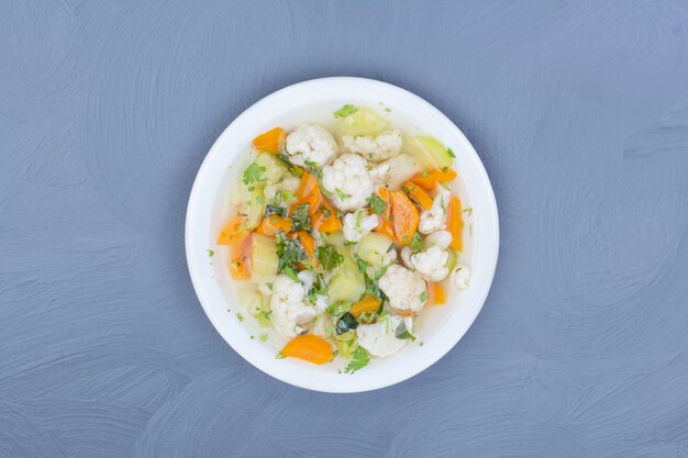 Broth soup with chopped and minced vegetables in a white plate.