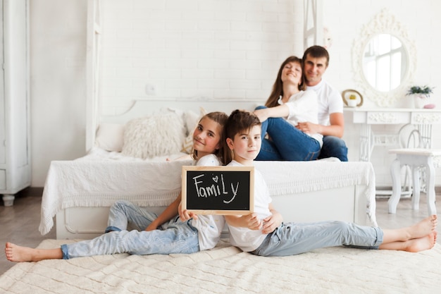 Brother and sister holding slate with family text sitting on carpet in front of their parent