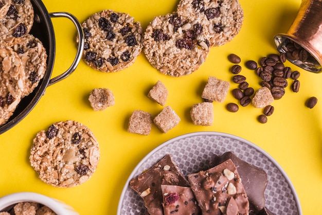 Brow sugar cubes; chocolate cookies; coffee beans and chocolate bars plate on yellow bright backdrop