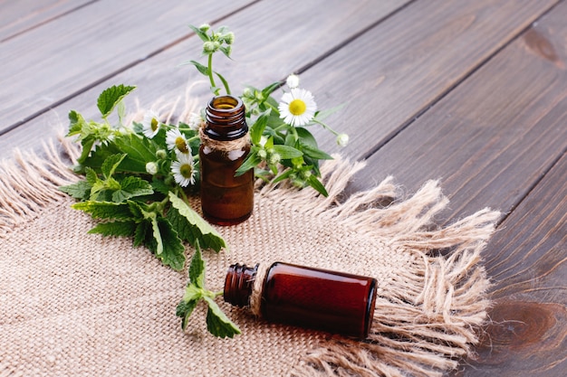 Brown bottles with oils, greenery and flowers lie on brown napkin