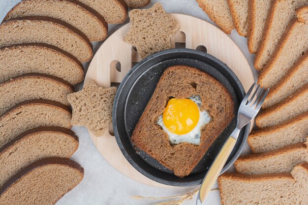 Brown bread with fried egg on dark pan .