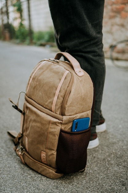 Free Photo brown canvas camera bag with a smart phone in the side pocket, on the ground