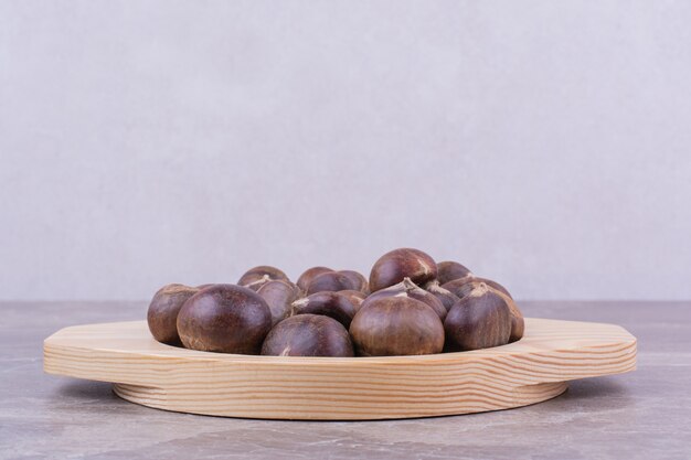 Brown chestnuts in a wooden platter on marble.