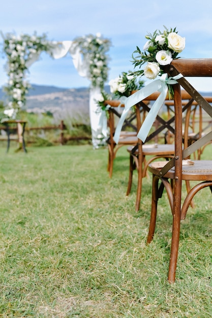 Free photo brown chiavari chairs decorated with white eustomas on the grass and the decorated wedding archway on the background