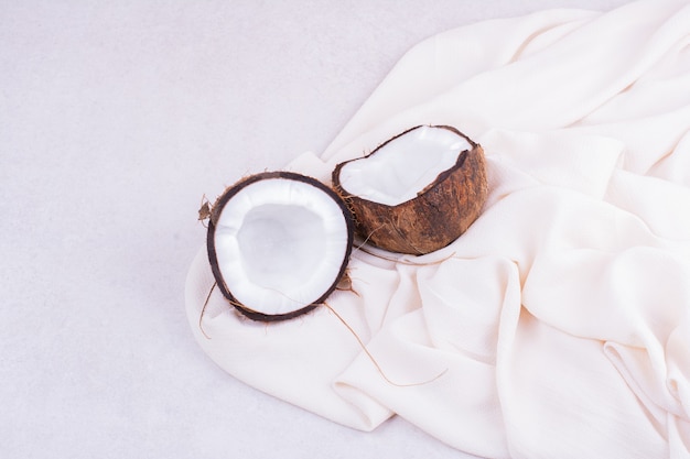 Free photo a brown coconut cut into two pieces on a white towel